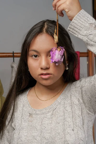 young latin woman with black hair, holding a purple rose on her head in her eye zone, studio with beauty and colorful nature, youth model