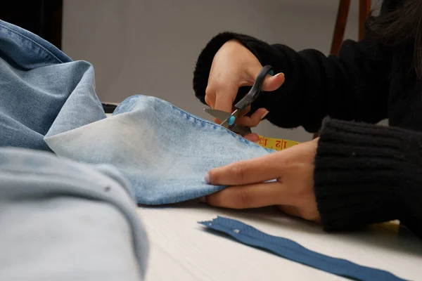 hands remodeling clothes, cutting jean fabric with scissors, on a work table, sewing instruments, craft occupation and wallpaper