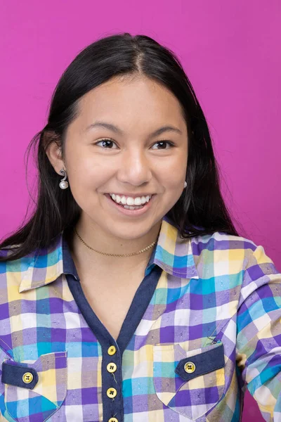 face of young latin girl with asian features with long black hair and a plaid shirt, model beauty smiling in studio with colorful background