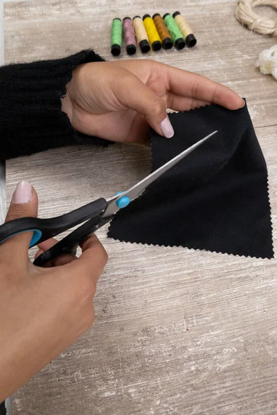 workplace, hands cutting with scissors a piece of black fabric for design, sewing and art in studio, objects as a background