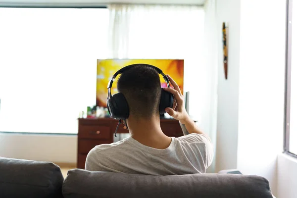 Arka koltukta oturan kişi bir evin oturma odasında kablosuz kulaklık kullanarak televizyon karşısında müzik, teknoloji ve hobileri olan bir yaşam tarzı dinliyor.