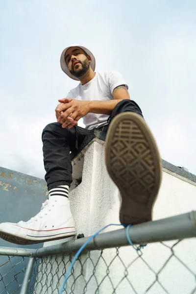 Latin young man with black hair and beard wears comfortable and casual clothes sitting with heaven in the background, lifestyle and urban fashion, male model