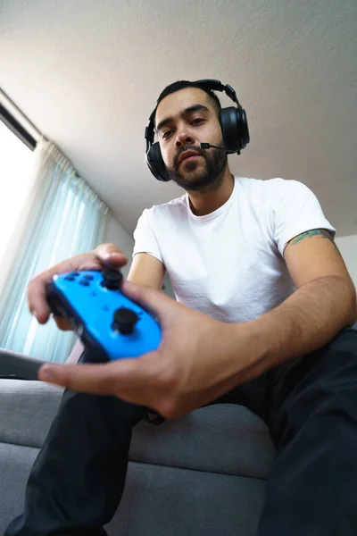 Young man with black hair and beard holding console control and gauges, Gamer\'s lifestyle resting on the sofa of the room, video games