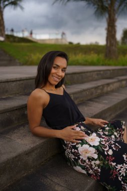 smiling brunette latin woman with short black hair posing resting on some bleachers, youth lifestyle, beauty and fashion in a park