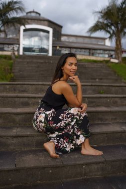 young model lifestyle sitting on a bleachers wears a long summer dress, beauty and fashion in the city