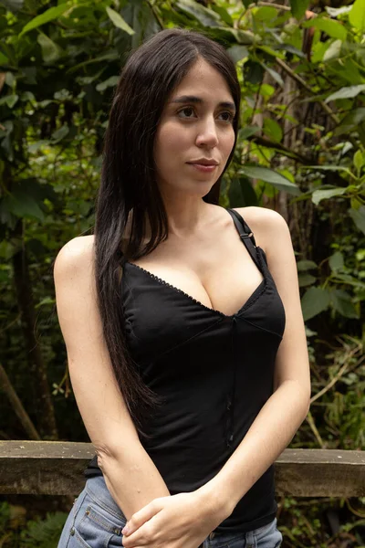 standing young woman with black hair wearing a black blouse, nature and beauty of latin model in a park, lifestyle of latin model