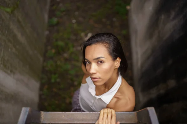 young brunette woman holding on to a ladder, natural beauty with detail on her face, latin model, daytime lifestyle