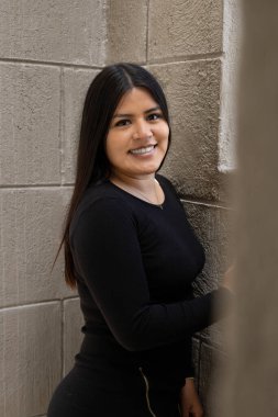 Smiling a young Latin woman with long and smooth hair, wears black clothes, next to a window in the day, lifestyle and beauty with makeup