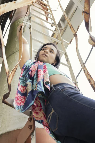 posing on stairs a beautiful Latin woman with short hair using a colored shirt and jeans, youth fashion in trend, lifestyle and beauty