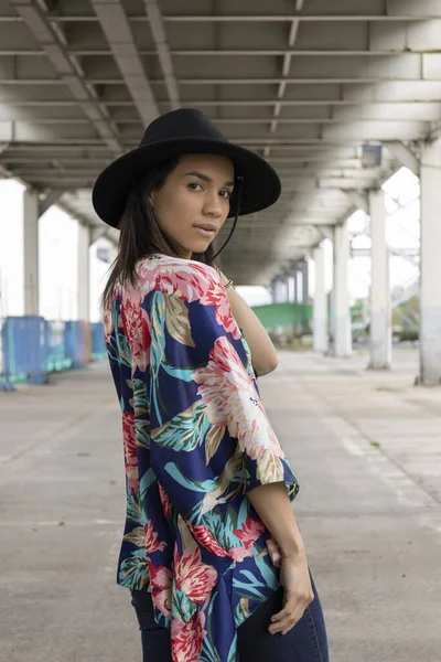 urban fashion of young latin brunette woman, natural beauty with fashionable accessories, portrait of female model, wearing as accessory a black hat and colorful kimono