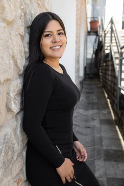 posing leaning against a stone wall beautiful young slim woman conc long hair wear black elegant dress, beauty with natural makeup in the city