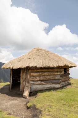 rustic hut with thatched roof and wooden structure, traditional architecture in the countryside, landscape with sky and clouds on a sunny day