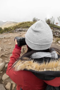 person wearing a wool cap is holding a camera and taking photo of rural scene, lifestyle and hobbies with modern technology