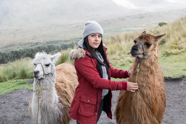young woman wearing a wool cap and jacket next to llamas, mammal domestic animal, nature scene in the countryside, farm lifestyle, tourist