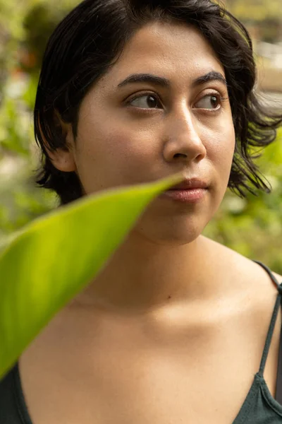details of the face of a young latin woman with short hair, smiling with a leaf in the shot, natural beauty in studio, close up to eyes, nose and lips