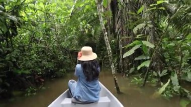 traveling in a canoe through a swamp in the middle of the jungle, wild nature and traditional and rustic means of transport with a seated tourist enjoying the landscape