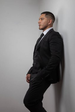 Duvara yaslanmış, kısa saçlı, iş adamı ve modern yaşam tarzı olan genç bir Latin, gömlek ve kravatlı zarif bir şekilde giyinmişti.