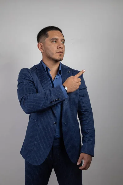 portrait of young latin man with short hair wears formal clothes, a suit, shirt and tie, study details of the face, successful business person pointing with his finger