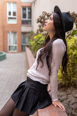 Uzun dalgalı saçlı, şapkası, yaşam tarzı ve gençlik modası olan genç bir Latin kadın profilinde dinleniyor.