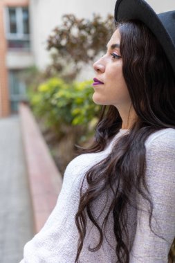 Uzun dalgalı saçlı, rahat etek, süveter ve şapka giyen, gündüzleri gençlik yaşam tarzı ve modası olan genç Latin bir kadın dinlenirken gülümsüyor.