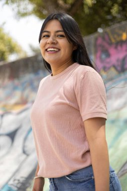 Güneşli bir yaz gününde doğal makyajlı ve uzun düz saçlı güzel bir kadın parkta gülümseyen basit bir tişört giyer.