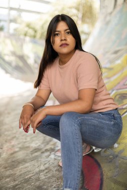 Güneşli bir yaz gününde doğal makyajlı ve uzun düz saçlı genç bir kadın çömelmiş poz veriyor, rahat bir tişört giyiyor, yaşam tarzı.