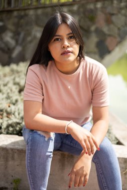 Doğayla bir parkta poz vermek, uzun düz saçlı genç bir kızın yaşam tarzı, basit bir tişört giyer, Latin bir kadının güzelliği.