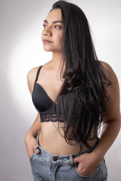 studio portrait photo of a latin young woman with long hair and brunette skin, wears a bra and jeans, casual and sensual fashion, natural beauty