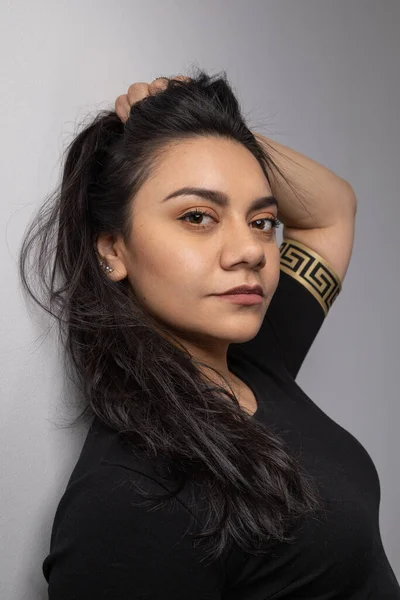 face of young latin woman holding her black hair, natural beauty with details in lip, eyes and nose, studio shot