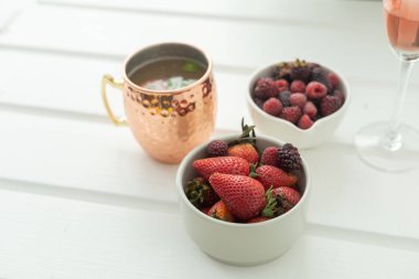 Masada sunulan taze kırmızı meyveler, çilekler ve böğürtlenler stüdyoda bir bardak soğuk içecekle sağlıklı yiyecekler, organik yiyecekler.