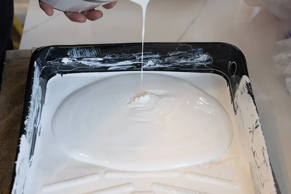 white paint is poured into a paint tray from a paint bucket