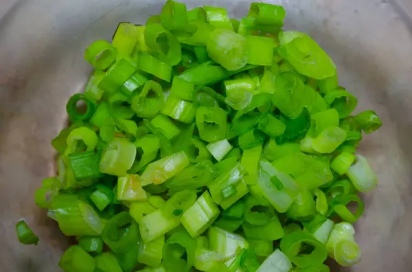 Fein geschnittene grüne Zwiebeln in einer Glasschüssel auf einem hellen Tisch in Großaufnahme — Stockfoto