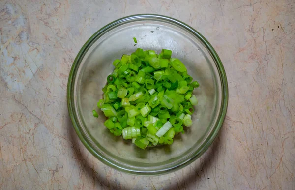 Jemně nakrájené zelené cibule ve skleněné misce na světlém stole — Stock fotografie