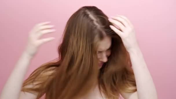 Menina bonita tenta pentear o cabelo com as mãos no fundo rosa. — Vídeo de Stock
