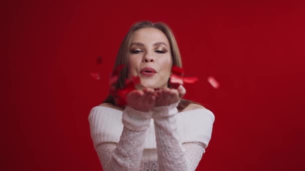 Молода мила жінка дме конфетті з її долонь на червоному тлі . — стокове відео