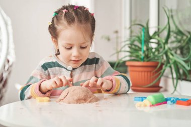 Renkli kazaklı küçük kız evde kinetik kumla oynuyor..
