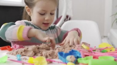 Renkli kazaklı küçük kız evde kinetik kumla oynuyor..