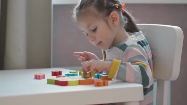 Little girl in colorful sweater plays with wooden puzzle at home. — Stock Video