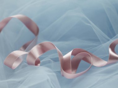 Tozlu pembe kıvrımlı saten kurdelenin yakın çekimi. Tül kumaş üzerinde açık pembe, ince kıvrımlı kurdele. Pastel renkler. Paketleme dekorasyonu