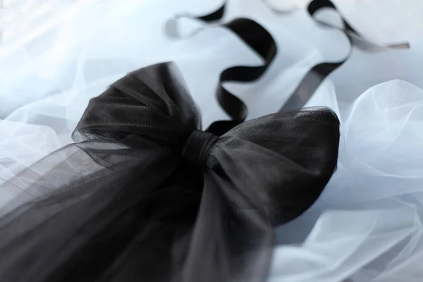 Black tulle bow belt with satin ribbon on blue backgroung. Diagonal black bow with curly satin ribbon top view