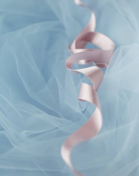 Baby pink curly satin ribbon on pastel blue tulle, top view. Light blue background. Wrapping decoration on tulle fabric