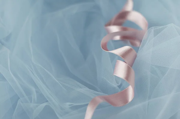 Light-pink silk satin ribbon curled in spirals on light-blue background. Wrapping decoration on tulle fabric. Packaging process