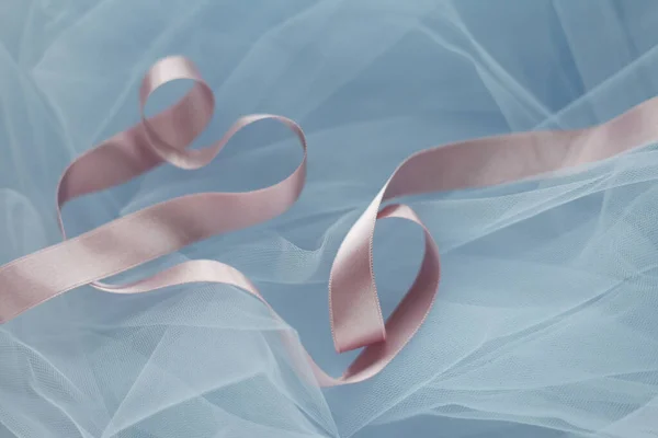 Curly baby pink satin ribbon twisted on baby blue tulle fabric background. Wrapping decoration on blue background