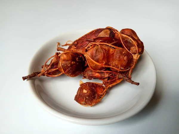 Wet and sticky tamarind or Tamarindus indica, after peeled. Fruit stalk still included. On a plate. Isolated in white background