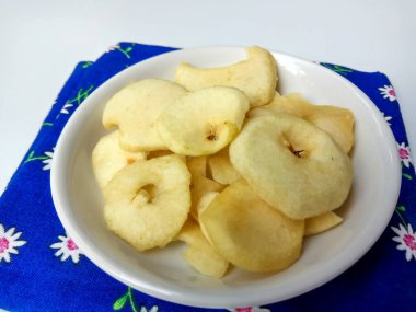 Kalın dilimlenmiş elma parçacıkları küçük beyaz tabakta, mavi peçeteli, beyaz arka planda izole edilmiş.