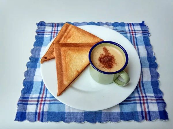 Triangular toasts and a cup of coffee, served on a white plate. Coffee inside a green enamel mug. Simple and classic style of breakfast