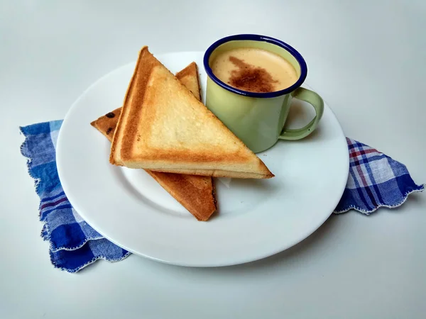 Triangular toasts and a cup of coffee, served on a white plate. Coffee inside a green enamel mug. Simple and classic style of breakfast