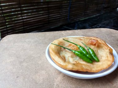 Piya pia udang, Semarang, Endonezya kökenli. Kızarmış un hamurundan karidesle yapılan tuzlu aperatif. Üç parça yeşil biber kağıdıyla servis edilir, beyaz tabakta, ahşap yüzeyde.