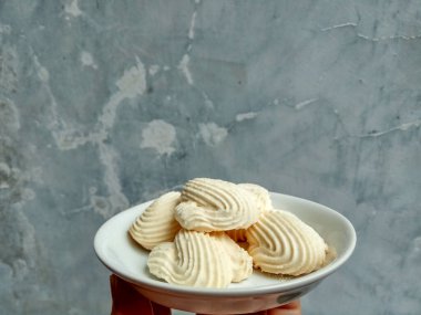 Spritz kurabiyeleri, ya da muhallebi kurabiyeleri ya da Endonezya dilinde roti semprit. Midye kabuğu şeklinde kurabiyeler. Beyaz küçük tabağın içine yerleştirilmiş.