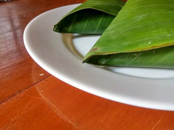 豆类制品 加工后的豆制品 用香蕉叶包裹 呈三角形 放在白色板上 有木制背景 — 图库照片